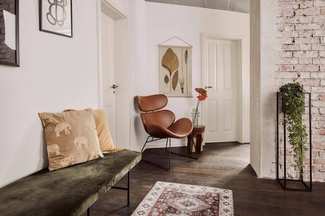Décoration éclectique avec banc en velours vert, fauteuil en cuir marron, métal noir et bois brut