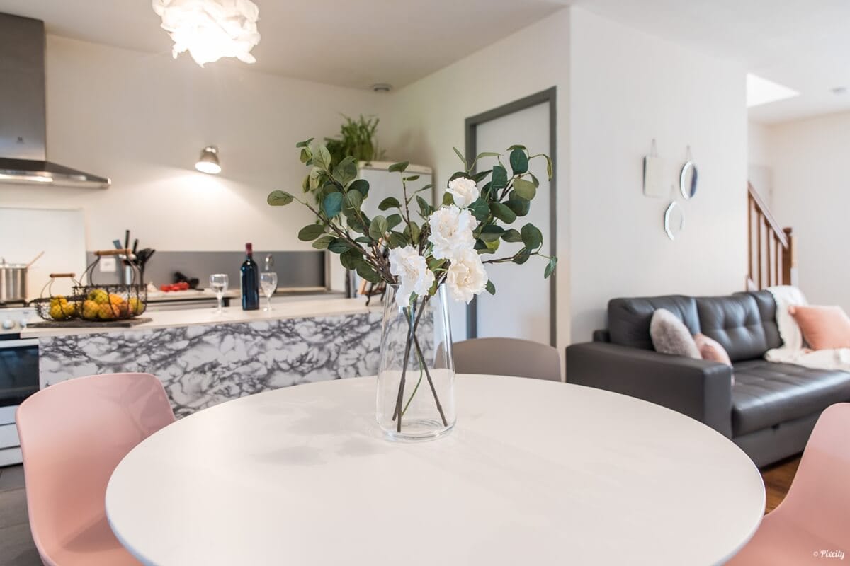 Pièce de vie ouverte avec cuisine, table à manger ronde et salon, organisée en plusieurs espaces.