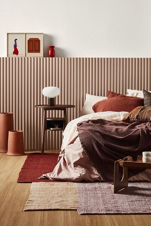 Chambre avec tapis superposés, linge de lit moelleux et coussins dans des tons ocre, jaune et prune